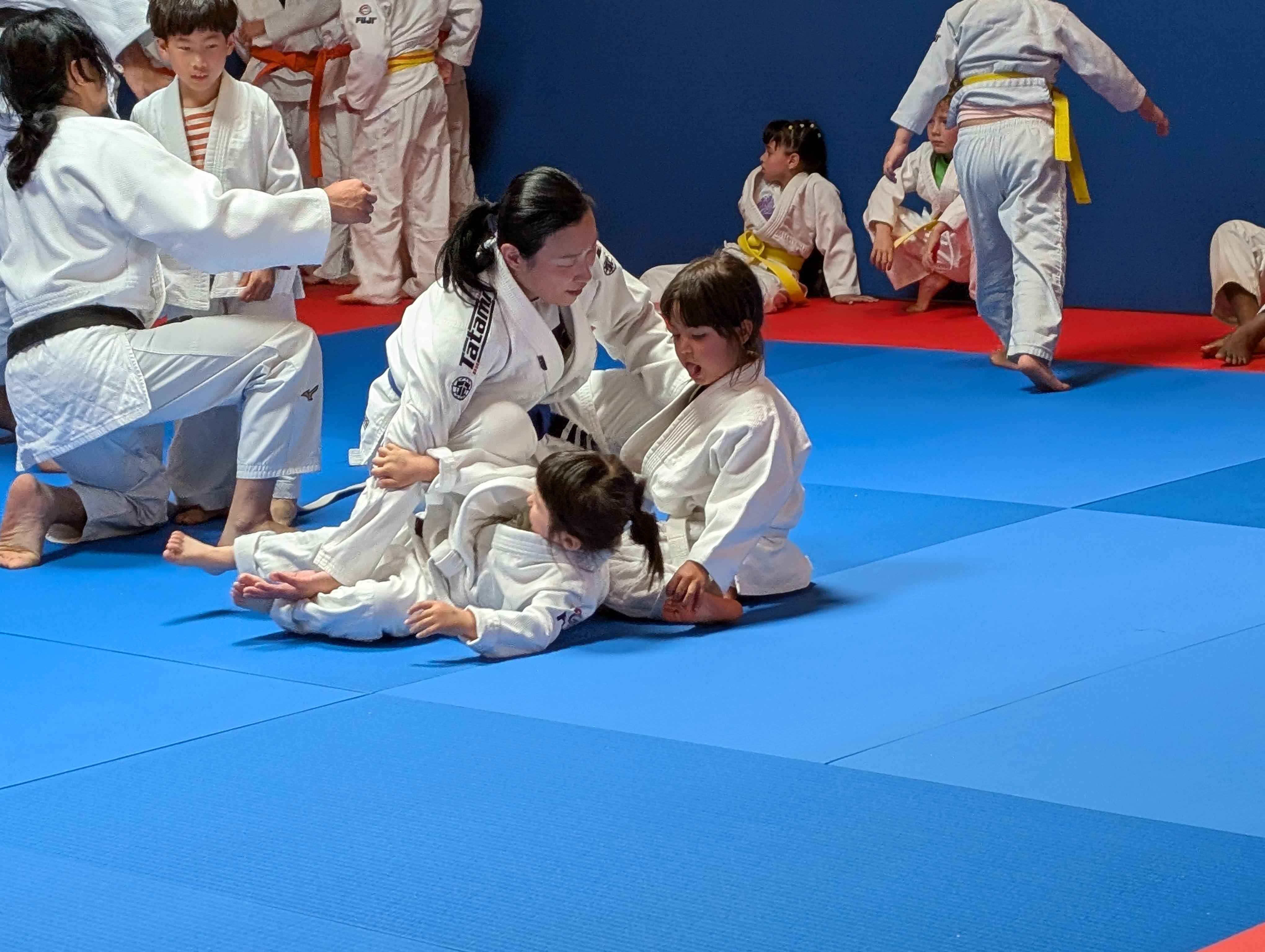 Lulu on the mats in a Brazilian Jiu Jitsu class with a group of children in white gis.